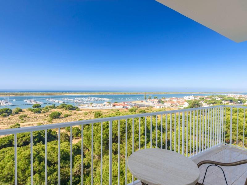 Blick von Balkon mit Geländer auf grüne Landschaft, Meer und blauen Himmel im Hintergrund.