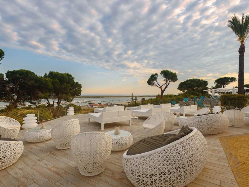 Offener Terrassenbereich mit weißem Rattanmöbel, Palmen und Blick auf das Meer bei Sonnenuntergang.