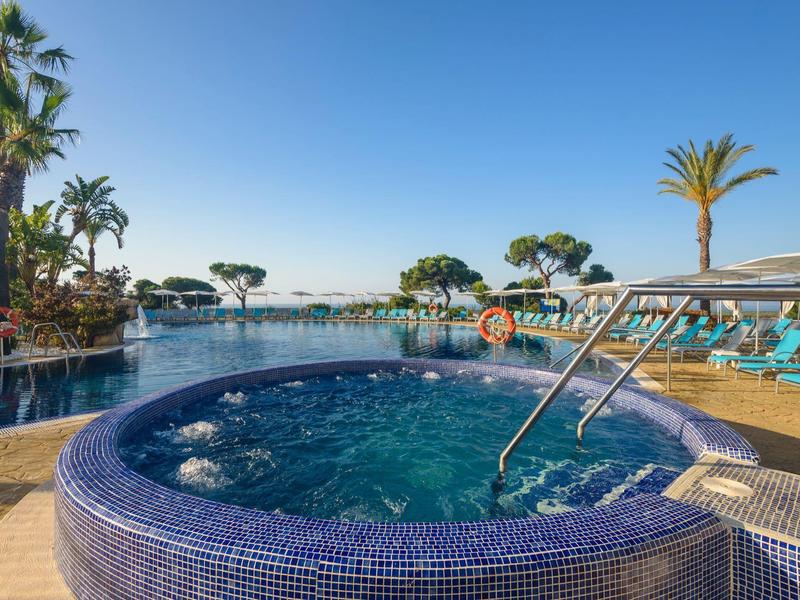 Runder Whirlpool mit blauen Mosaikfliesen an luxuriösem Pool mit Liegestühlen und Palmen.