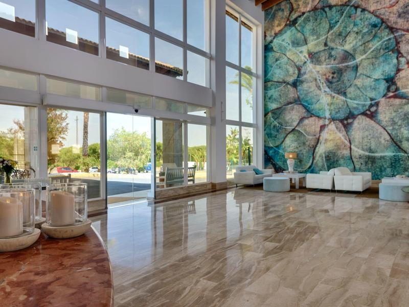 Großer heller Raum mit Marmorboden, großem Fenster und bunter Wandgestaltung, weiße Sitzmöbel.