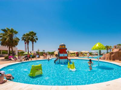 Runder Pool mit Wasserrutsche und Liegestühlen in einer sonnigen Hotelanlage.
