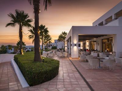 Hotelterrasse mit Sitzbereichen und Palmen bei Sonnenuntergang