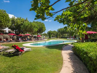 Ein Hotelgarten mit Pool, Liegestühlen und Sonnenschirmen an einem sonnigen Tag.