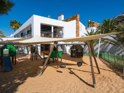 Hotel moderno sulla spiaggia con area giochi sabbiosa e tende da sole davanti all'edificio.