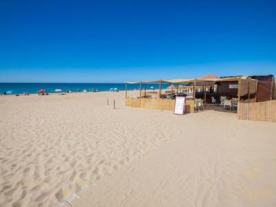 Breiter Sandstrand mit klarem blauen Himmel und Strandbar am rechten Rand.