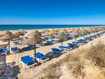 Strand mit Reihen von blauen Liegestühlen und Strohhüten unter klarem blauem Himmel.