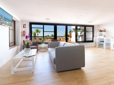 Helles Wohnzimmer mit grauem Sofa, großem Fenster und Blick auf Palmen und Meer.