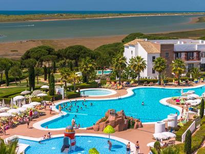Grande piscina del resort con molti ospiti, circondata da lettini e palme vicino alla spiaggia.