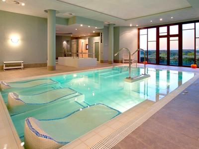 Piscina interna con lettini e ampie finestre che si affacciano su un paesaggio al tramonto.