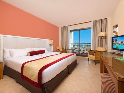 Camera d'hotel luminosa con letto grande, scrivania e balcone con vista mare.