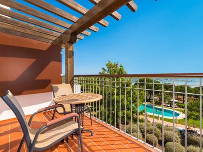 Balcone con tavolo e sedie che si affaccia sulla piscina e sul mare sotto un cielo sereno.