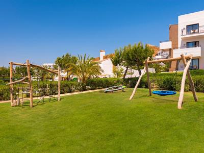 Giardino verde con altalene e struttura per arrampicata davanti a un hotel sotto il cielo sereno.