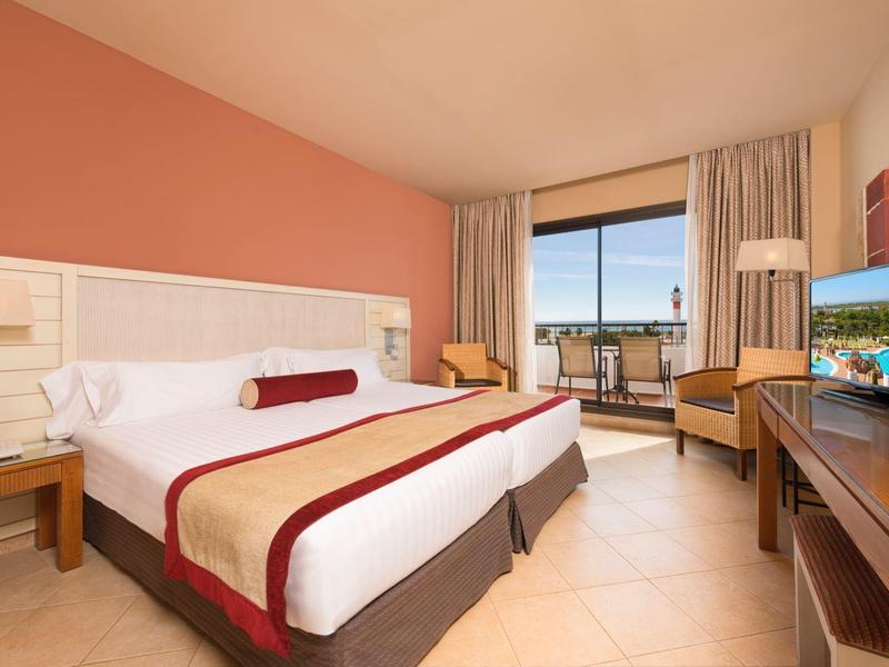 Camera d'hotel luminosa con letto grande, scrivania, TV e balcone con vista sul mare.