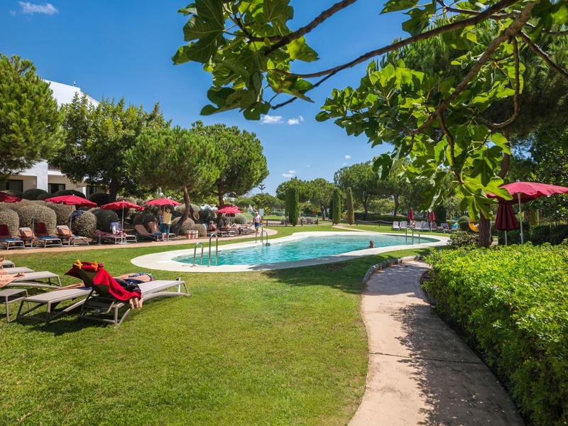 Piscina con lettini e ombrelloni rossi in un'area verde dell'hotel in una giornata di sole.