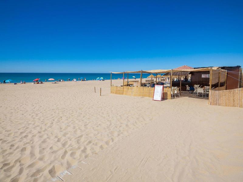 Spiaggia sabbiosa con bar sulla spiaggia, cielo azzurro e persone vicino al mare