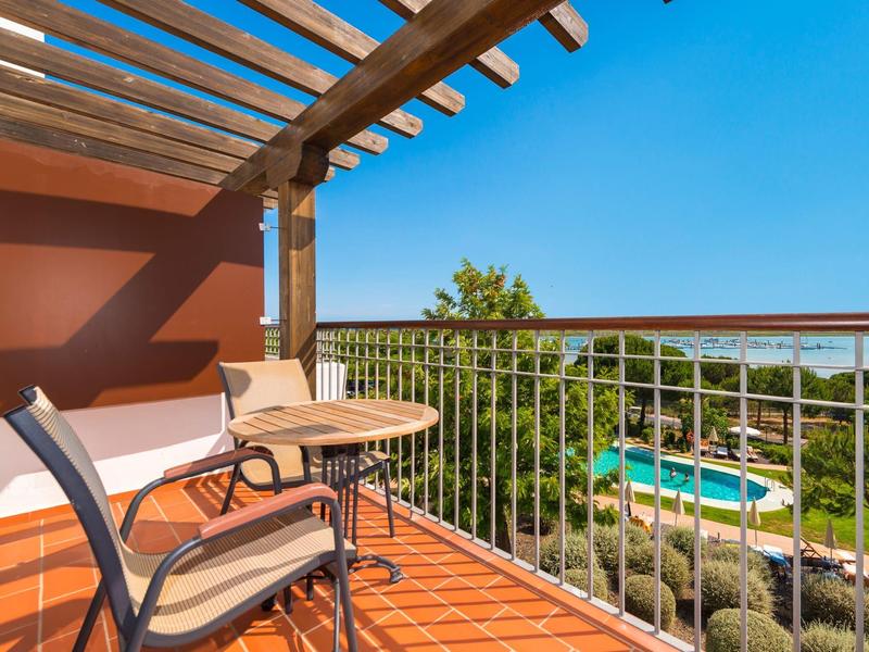Balcone con tavolo e sedie che si affaccia sulla piscina e sul mare sotto un cielo sereno.