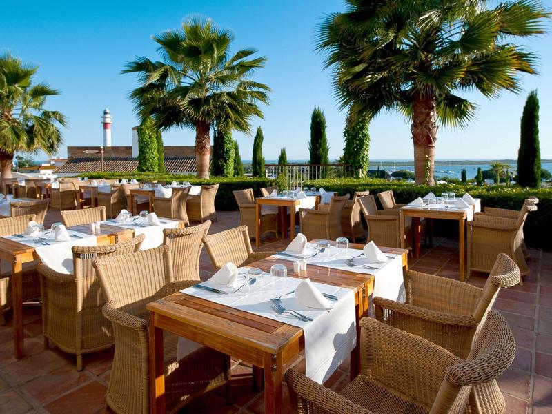 Elegante area esterna con tavoli apparecchiati e palme sotto un cielo sereno.