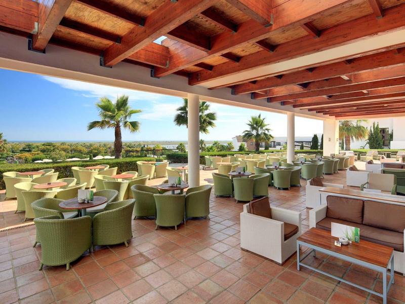 Terrazza aperta dell'hotel con poltrone verdi vista mare e palme.