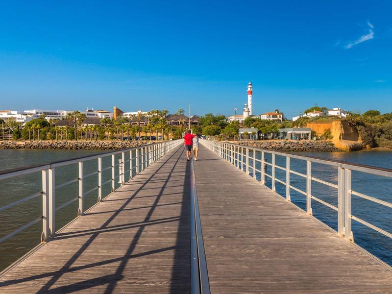 Una persona con una maglietta rossa cammina su un lungo ponte di legno con ringhiere sull'acqua.