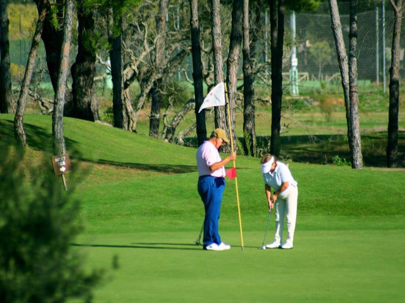 Due golfisti sul green, uno tiene la bandiera, l'altro si prepara a puttare.