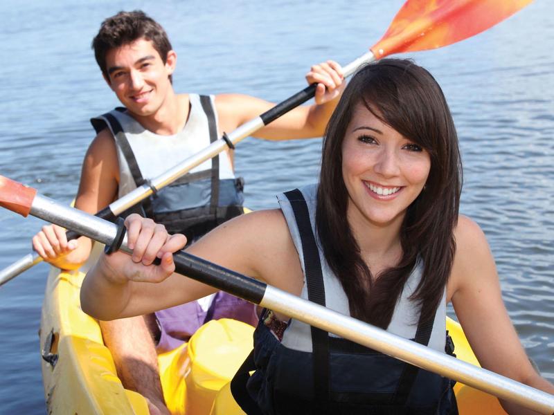 Due giovani sorridenti mentre fanno kayak su acque aperte.