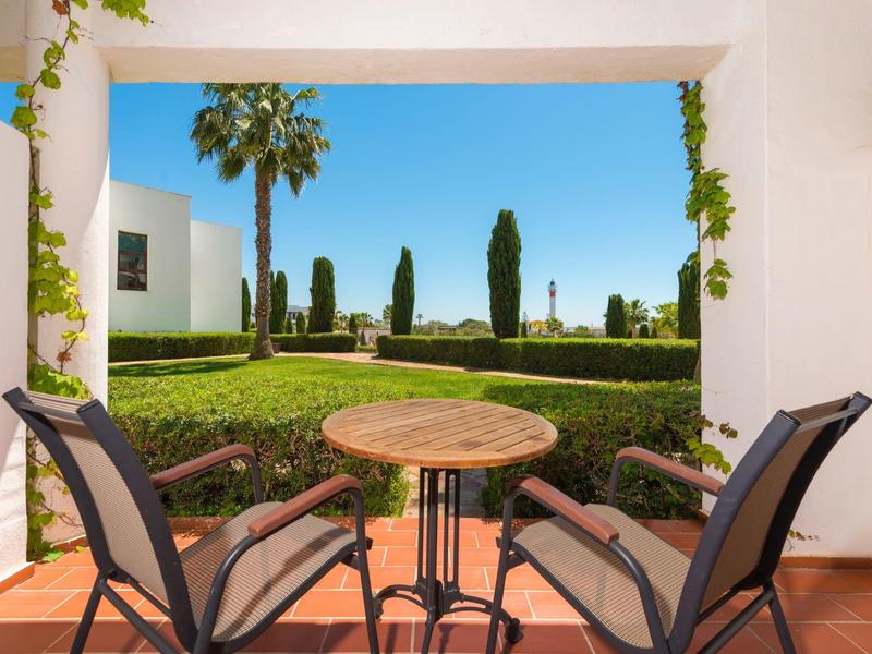 Terrazza con tavolo e sedie che si affaccia su palme e giardino verde sotto un cielo azzurro.