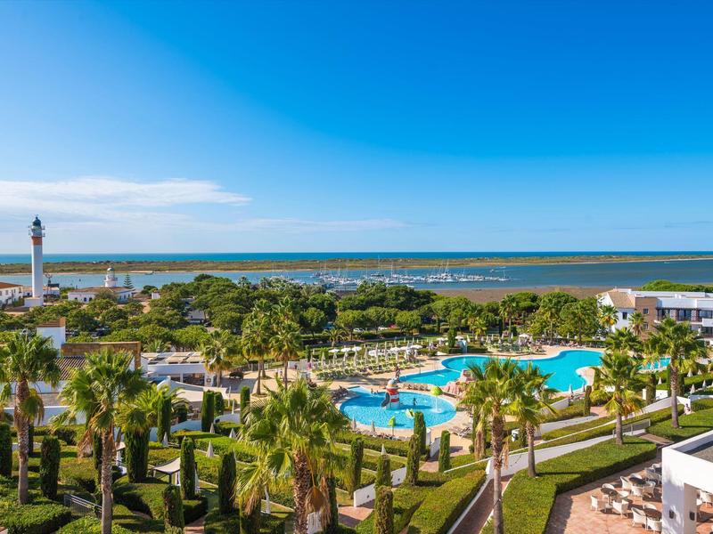 Vista della piscina dell'hotel, palme e faro vicino al mare sotto un cielo limpido