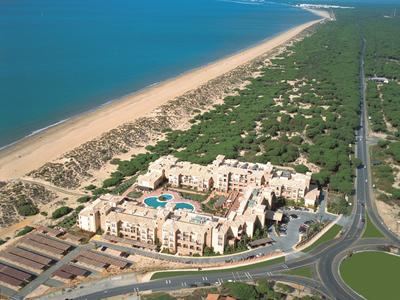 Blick auf ein Hotelresort mit Pool nahe einem langen Sandstrand und Waldgebiet.