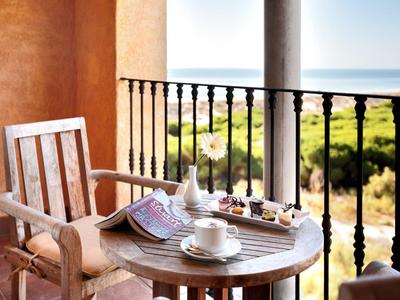 Houten tafel op balkon met theeset en gebakjes met uitzicht op groen landschap en oceaan.