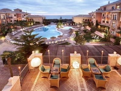 Luxe resort met groot zwembad, ligbedden, palmbomen en twee verdiepingen tellende gebouwen onder bewolkte lucht.