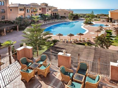 Gezellig terras met rieten stoelen met uitzicht op groot zwembad en zee bij hotel aan zee.
