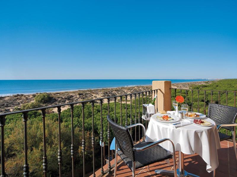 Balkon met tafel voor ontbijt, uitzicht op zee en groen landschap onder een heldere blauwe lucht.