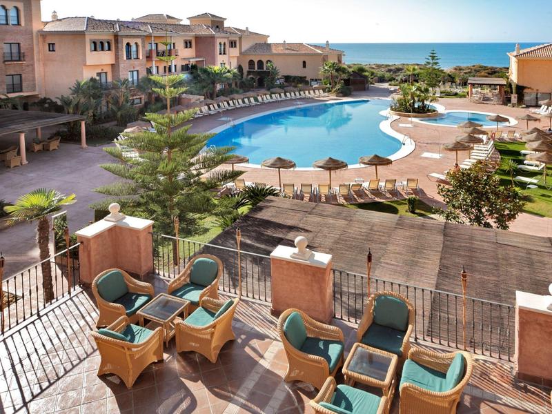 Gezellig terras met rieten stoelen met uitzicht op groot zwembad en zee bij hotel aan zee.