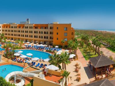Hell eingerichtetes Hotelzimmer mit Doppelbett, Nachttischen, Stuhl und Spiegelwand.