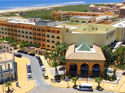 Große Hotelanlage mit gelben Gebäuden, mehreren Stockwerken und Blick aufs blaue Meer im Hintergrund.
