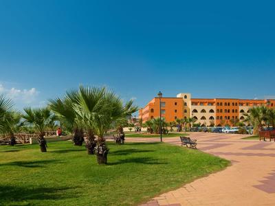 Budova hotelu vedle upravené zahrady s palmami a cestou pod modrou oblohou