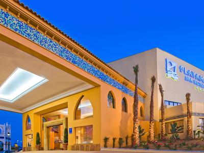 Moderní exteriér hotelu s teplým žlutým osvětlením a jasnou modrou oblohou.