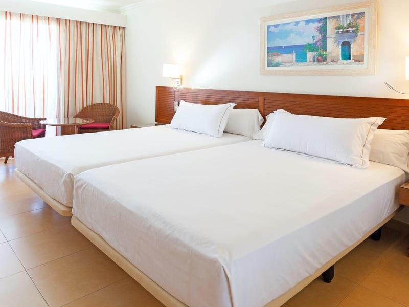 Helles Hotelzimmer mit zwei Einzelbetten, weißen Bettlaken, einem Tisch und zwei Stühlen am Fenster.