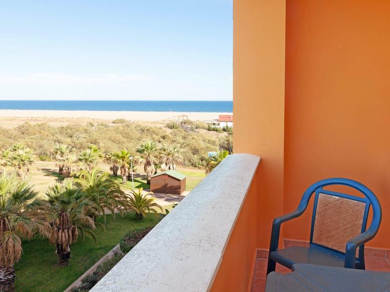 Balkon mit blauer Stuhl, orange Wände, Blick auf Palmen, Sanddünen und Blaues Meer.