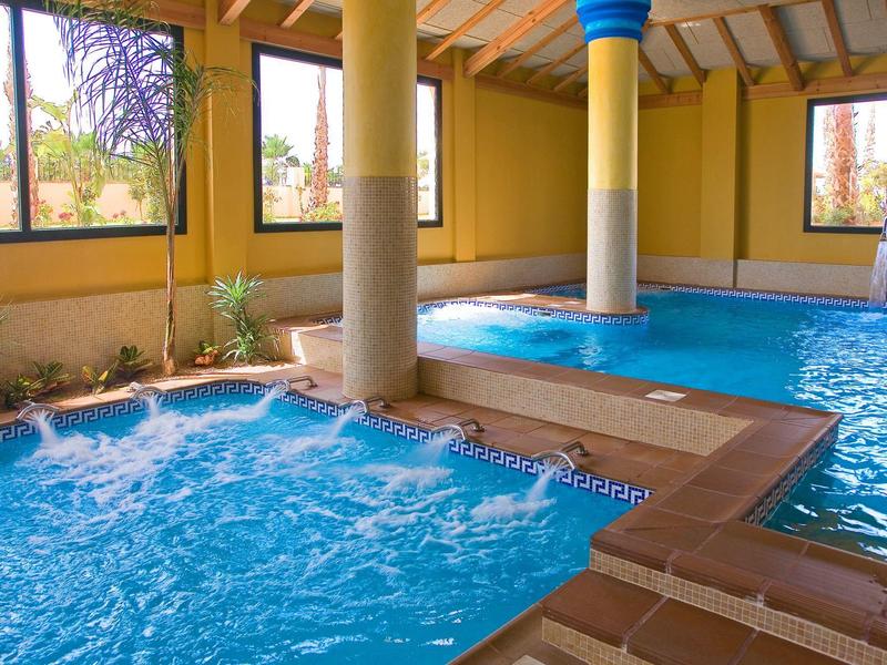 Hallenbad mit Whirlpool, gelben Wänden, großen Fenstern und Holzdecke mit Dachbalken.