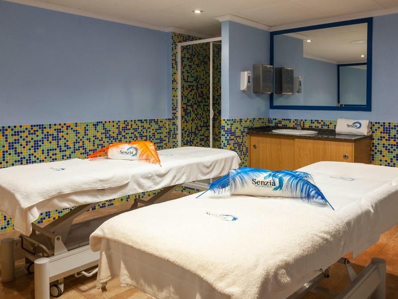 Ein ruhiger Massageraum mit zwei Liegen, blauen Wänden und bunter Wandfliese.