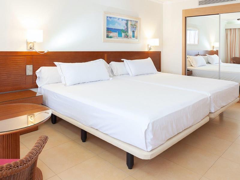 Hell eingerichtetes Hotelzimmer mit Doppelbett, Nachttischen, Stuhl und Spiegelwand.