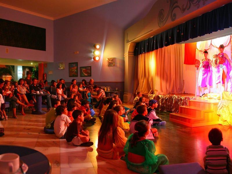 Kinder schauen auf einer Bühne einem Tanz in einem warm beleuchteten Saal zu.