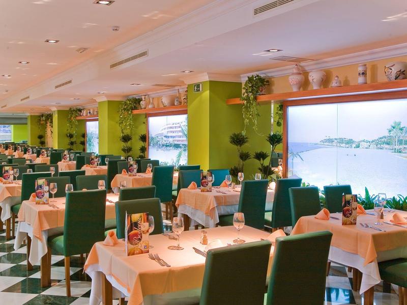 Großer, heller Speisesaal mit grün gepolsterten Stühlen und weißen Tischdecken auf schwarz-weißem Boden.