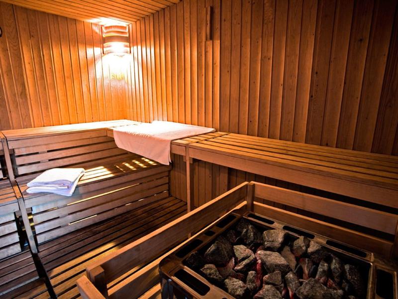 Überdachte Terrasse mit weißen Metalltischen und Stühlen, Boden aus grauem Beton, Palmen im Hintergrund.