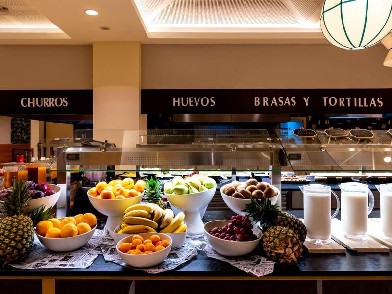 Buffet mit Schalen voll Obst, Körben mit Brot, und Behältern in einer warmen Restaurantküche.