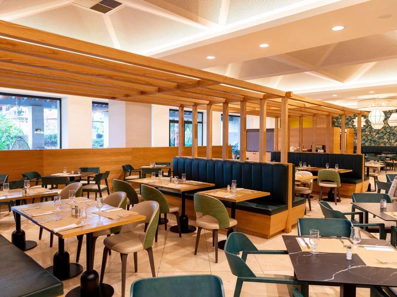 Modernes Restaurant mit Holzelementen, bequemen Sesseln und stilvollen Tischen, heller Raumgestaltung.