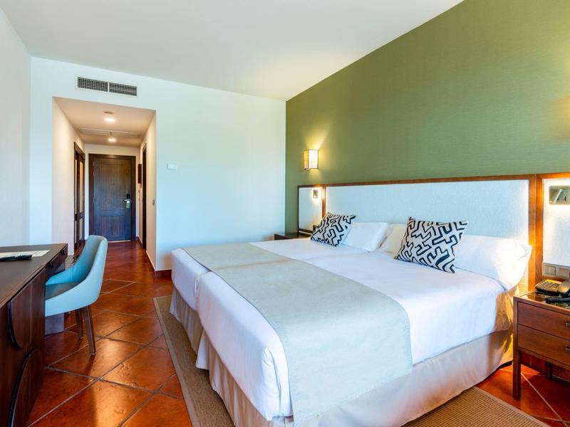 Modernes Hotelzimmer mit zwei Betten, grünem Akzent an der Wand und Holzfußboden.