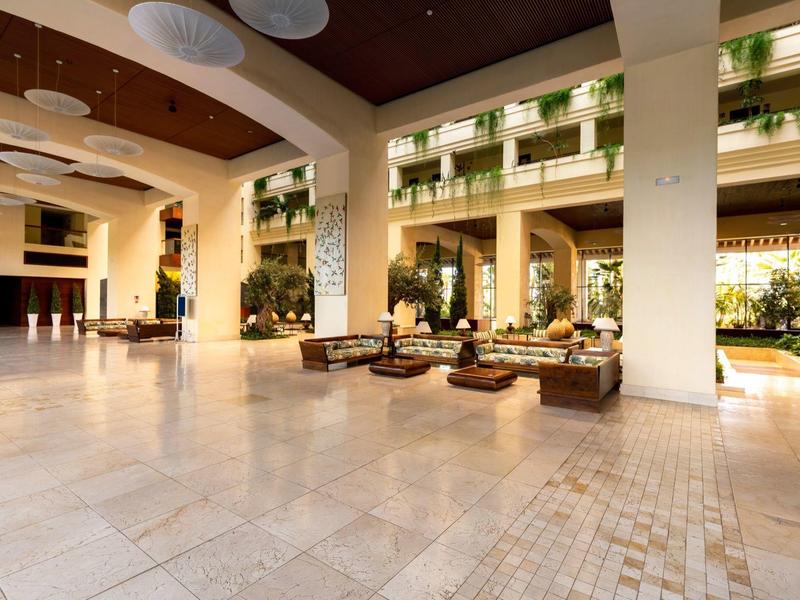 Große helle Halle mit bequemen Sitzbereichen, Deckengestaltung und Pflanzen auf Balkonen.