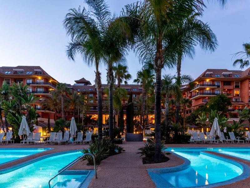 Resort mit Poolanlage, Palmen und mehrstöckigen roten Gebäuden bei Dämmerung.